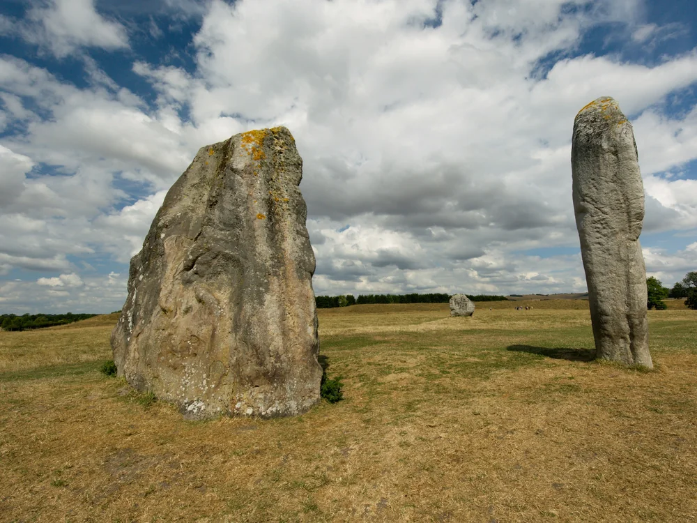 Two large sarsen standing stones in a grassy field at Avebury stone circle under a blue sky with clouds
